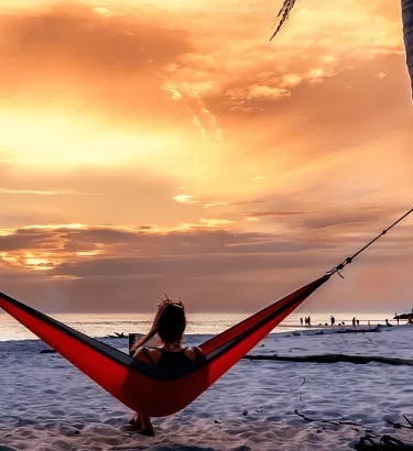 A person laying in a hammock at sunset