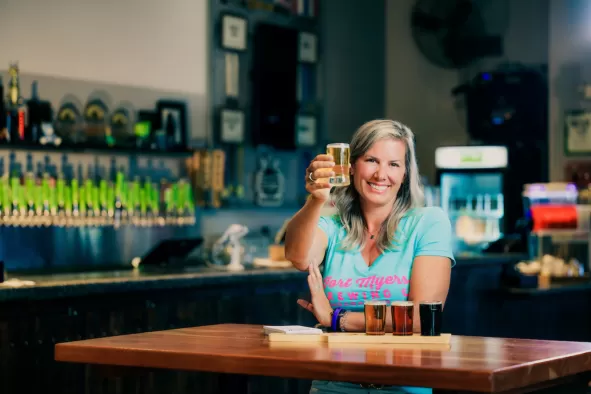 A woman holds a 5oz craft beer pour to cheers the camera